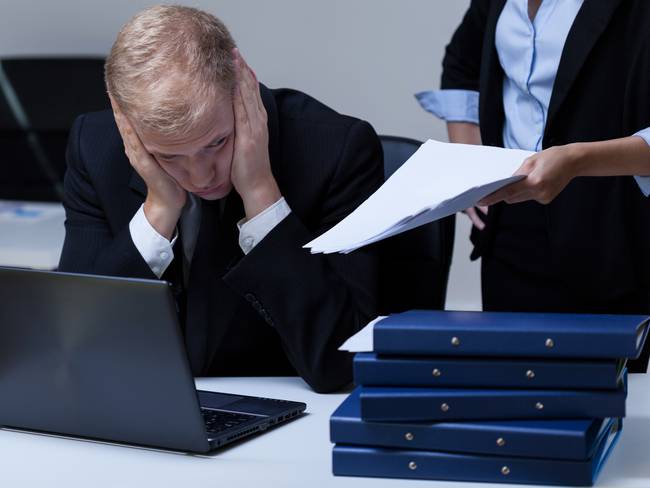 Hombre estresado y aburrido en el trabajo, mientras le entregan más tareas (Getty Images)
