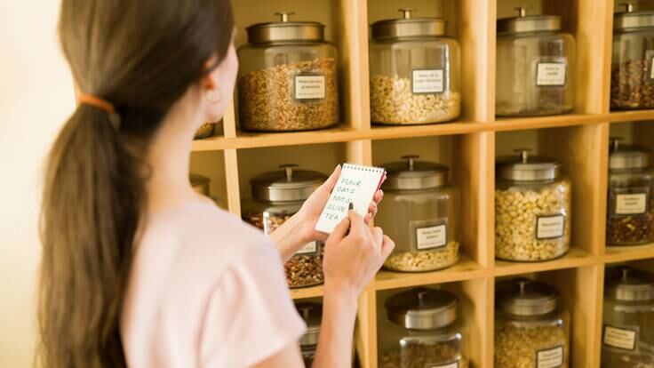 Mujer revisando una lista de compras, mientras observa una repisa con varios cereales (Getty images)