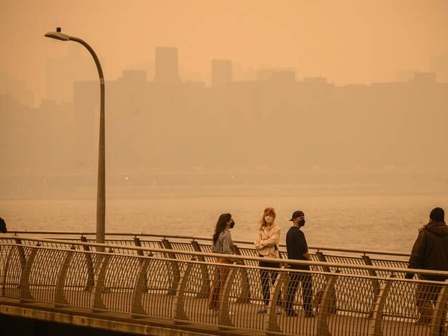 The Manhattan skyline is seen past people wearing face masks while walking along a pier as smoke from wildfires in Canada cause hazy conditions in New York City on June 7, 2023. An orange-tinged smog caused by Canada&#039;s wildfires shrouded New York on Wednesday, obscuring its famous skyscrapers and causing residents to don face masks, as cities along the US East Coast issued air quality alerts. (Photo by Ed JONES / AFP)