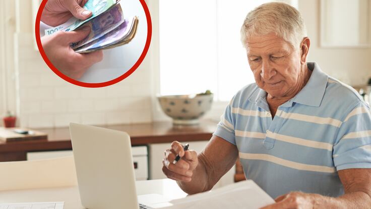 Hombre con una computadora y papeles sobre una mesa junto a unos billetes (Foto vía Getty Images)