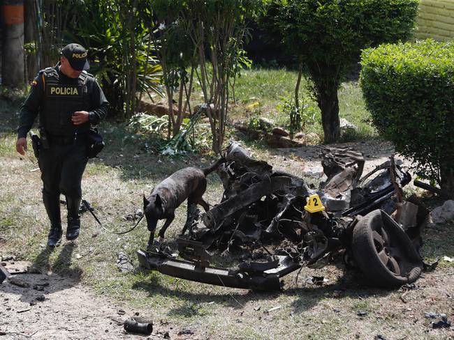 AME1786. JAMUNDI (COLOMBIA), 22/09/2023.- Un policía con un perro antiexplosivos inspeccionan los restos de un carro bomba, activado contra una subestación de policía hoy, en el corregimiento Potrerito, del municipio de Jamundí, Valle del Cauca (Colombia). Al menos cinco personas resultaron heridas este viernes en una zona rural del departamento del Valle del Cauca después de la explosión de un carro bomba en cercanías de una estación policial de la localidad de Jamundí, informó la Policía. EFE/Ernesto Guzmán