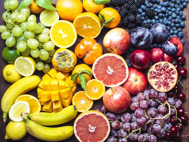Diferentes tipos de frutas enteras y cortadas sobre una mesa (Getty Images)