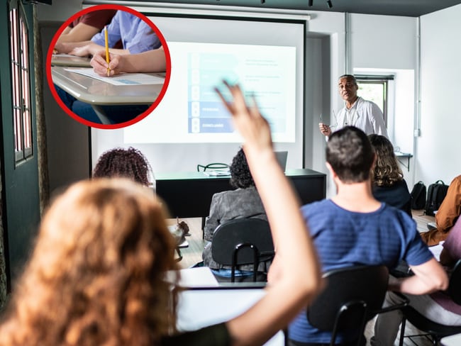 Aula con estudiantes y una mujer levantando la mano junto a alguien que resuelve una prueba (Getty Images)