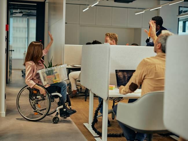 Mujer con situación de discapacidad despidiéndose de sus compañeros de trabajo  (Getty Images)
