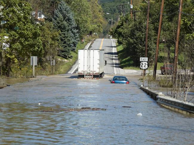 High water flash flooded highway emergency after a strong summer thunderstorm, one stranded car and a semi truck able to drive through amid floating debris, Pennsylvania, PA, USA.