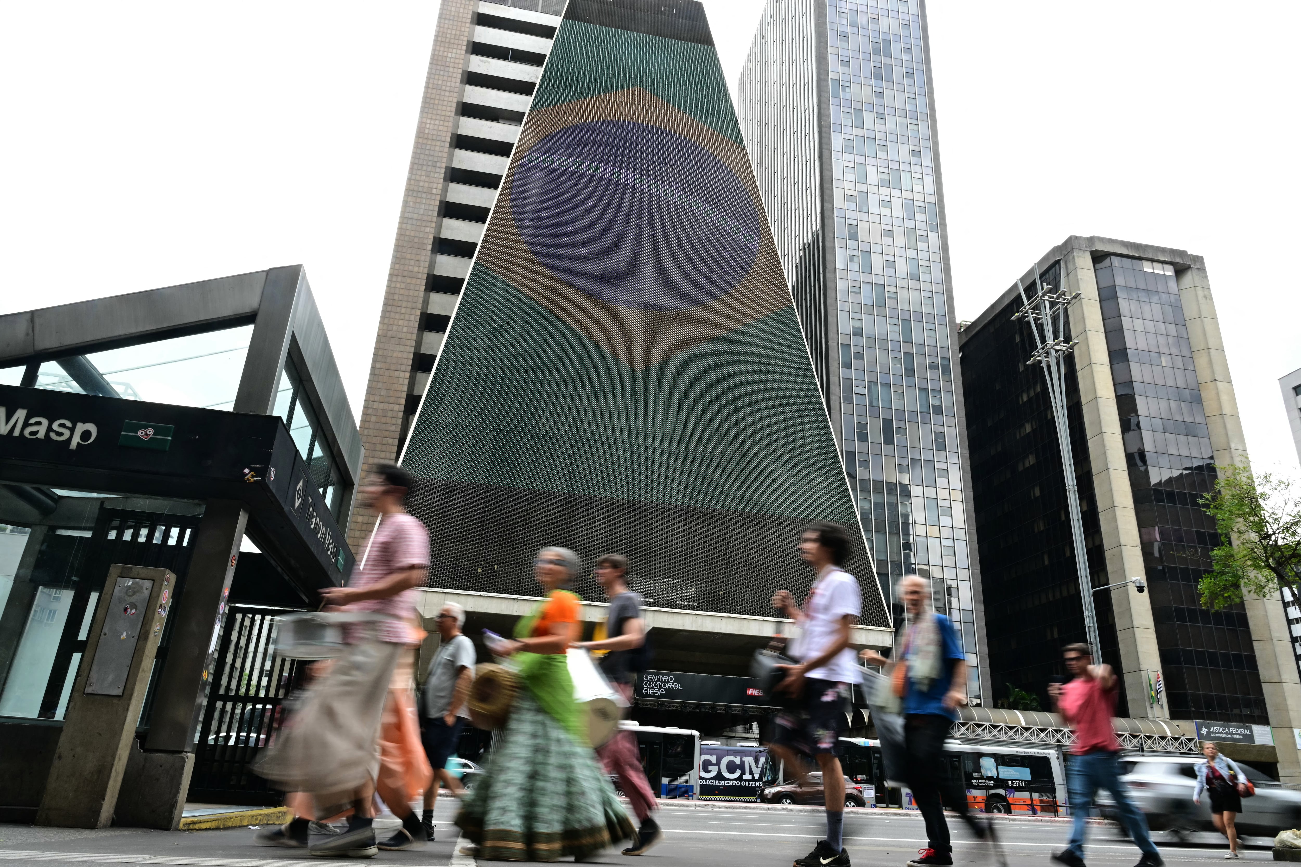 People walk past the Federation of Industries of the State of Sao Paulo (FIESP) building on Paulista Avenue in Sao Paulo, Brazil, on October 4, 2026, on presidential election day. Brazilians head to the polls in a highly polarized presidential election between incumbent leftist President Luiz Inacio Lula da Silva -seeking a fourth presidential mandate- and right-wing senator Flavio Bolsonaro, who emerged as the leading figure of the conservative movement following the conviction and imprisonment of his father, former president Jair Bolsonaro. (Photo by Pablo PORCIUNCULA / AFP)