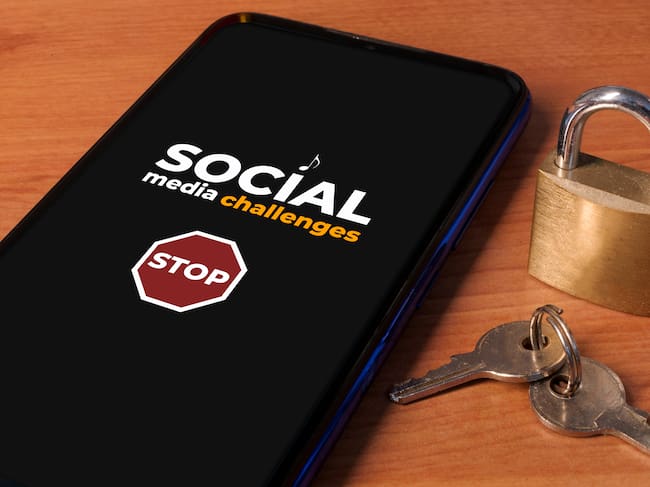 Smartphone showing the message "stop social media challenges" a wooden table with a lock and keys. Imagen tomada de Getty Imagenes (Crédito: Cristian Storto Fotografia)