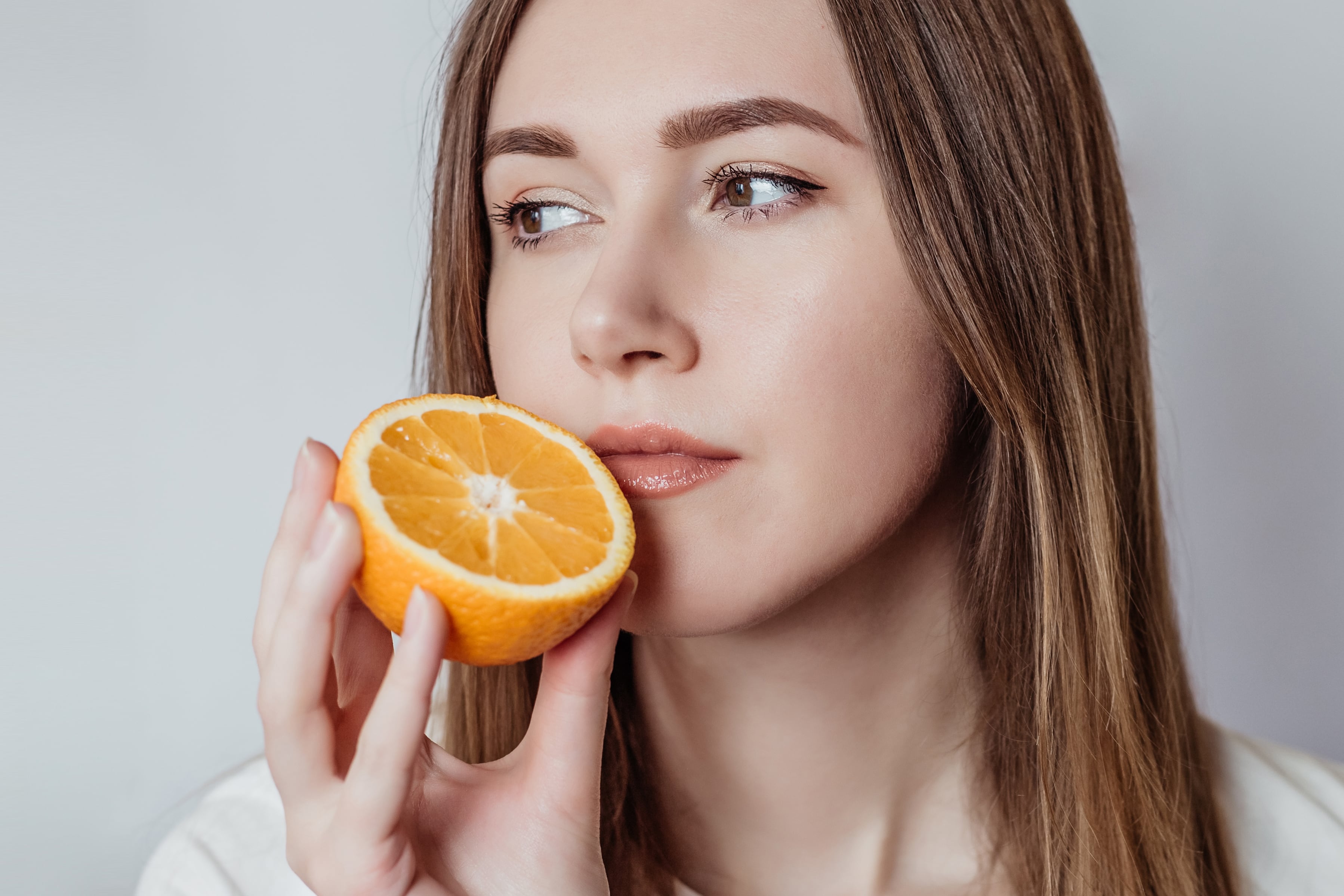 Loss of smell concept. Close up portrait of caucasian young woman holding an orange near her nose isolated over white background in the studio