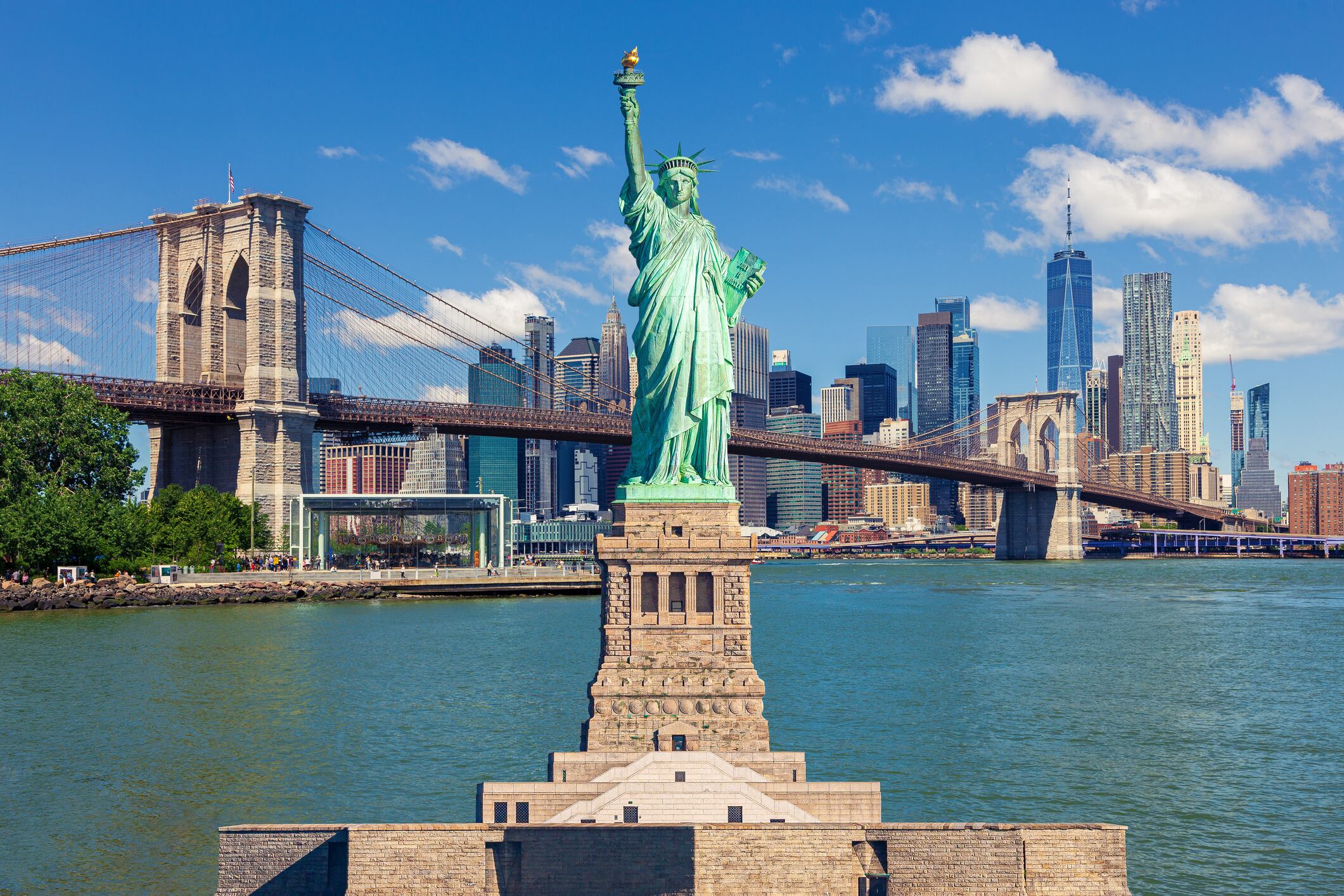 Estatua de la Libertad con el Puente de Brooklyn, rascacielos del distrito financiero del Lower East Side de Manhattan, World Trade Center, FDR Drive, Pier 17, Brooklyn Bridge Park y el cielo azul de la mañana con nubes hinchadas en el fondo, Nueva York. / Getty Images