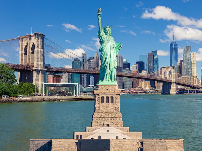 Estatua de la Libertad con el Puente de Brooklyn, rascacielos del distrito financiero del Lower East Side de Manhattan, World Trade Center, FDR Drive, Pier 17, Brooklyn Bridge Park y el cielo azul de la mañana con nubes hinchadas en el fondo, Nueva York. / Getty Images