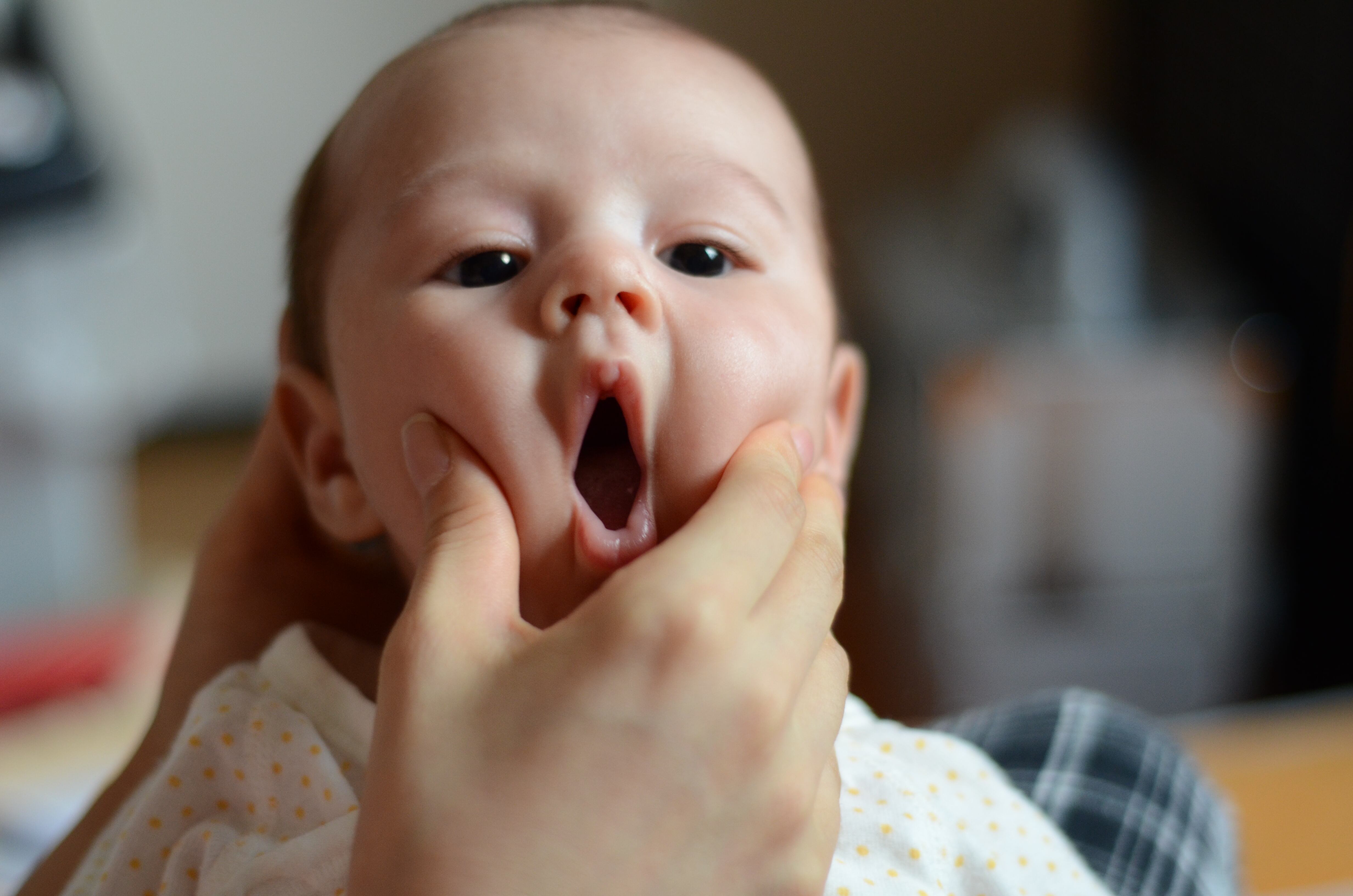Closeup of a baby boy having his cheeks squeezed until his mouth forms an "O."