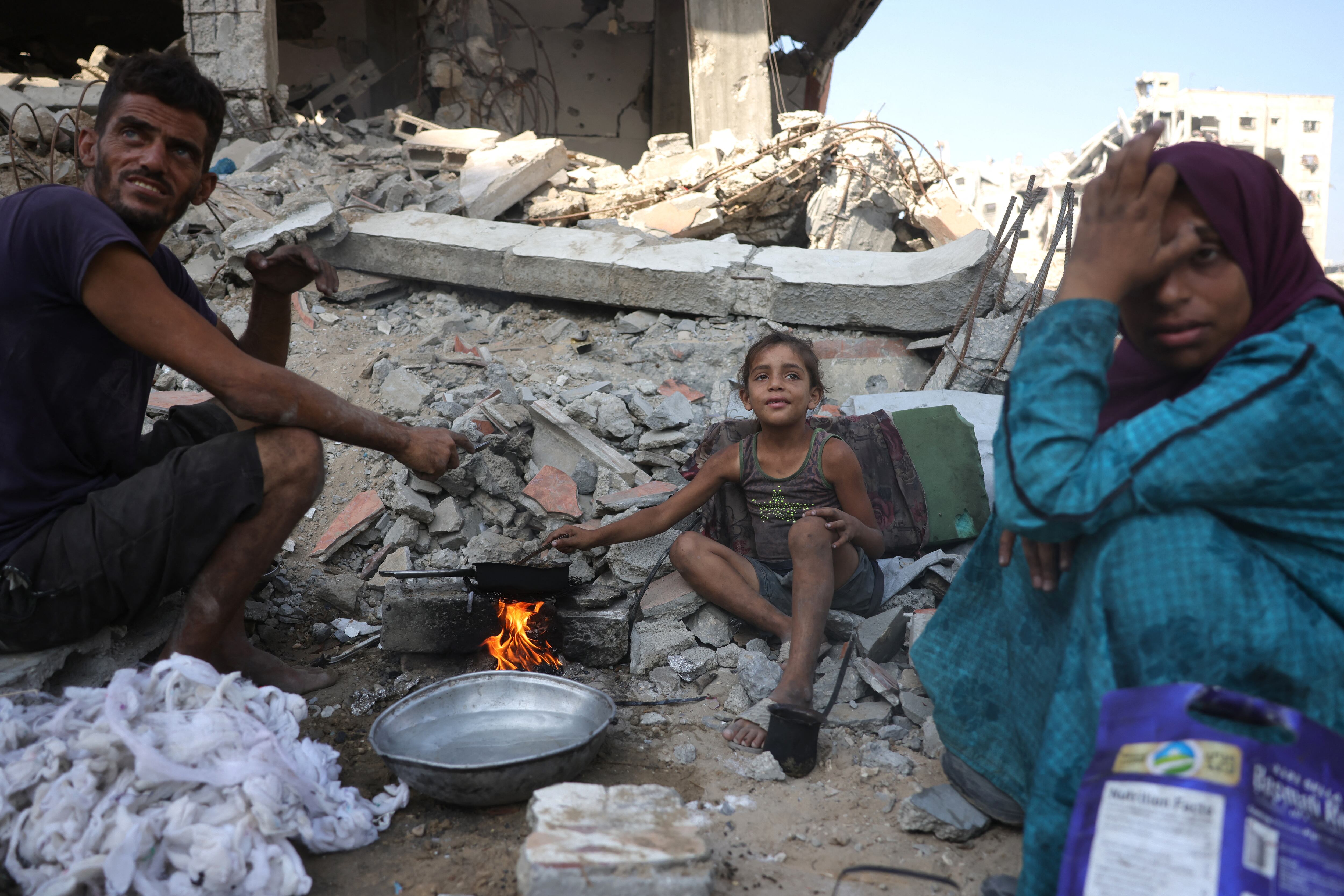 A displaced Palestinian man and his family warm up chickpeas as they sit amid the destruction in Saftawi neighbourhood, west of Jabalia in the northern Gaza Strip, on August 24, 2025, amid the ongoing war between Israel and the Palestinian Hamas militant group. The United Nations officially declared a famine in Gaza on August 22, blaming "systematic obstruction" of aid by Israel during more than 22 months of war, with Prime Minister Benjamin Netanyahu swiftly dismissing the findings. (Photo by BASHAR TALEB / AFP)