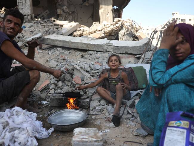 A displaced Palestinian man and his family warm up chickpeas as they sit amid the destruction in Saftawi neighbourhood, west of Jabalia in the northern Gaza Strip, on August 24, 2025, amid the ongoing war between Israel and the Palestinian Hamas militant group. The United Nations officially declared a famine in Gaza on August 22, blaming "systematic obstruction" of aid by Israel during more than 22 months of war, with Prime Minister Benjamin Netanyahu swiftly dismissing the findings. (Photo by BASHAR TALEB / AFP)