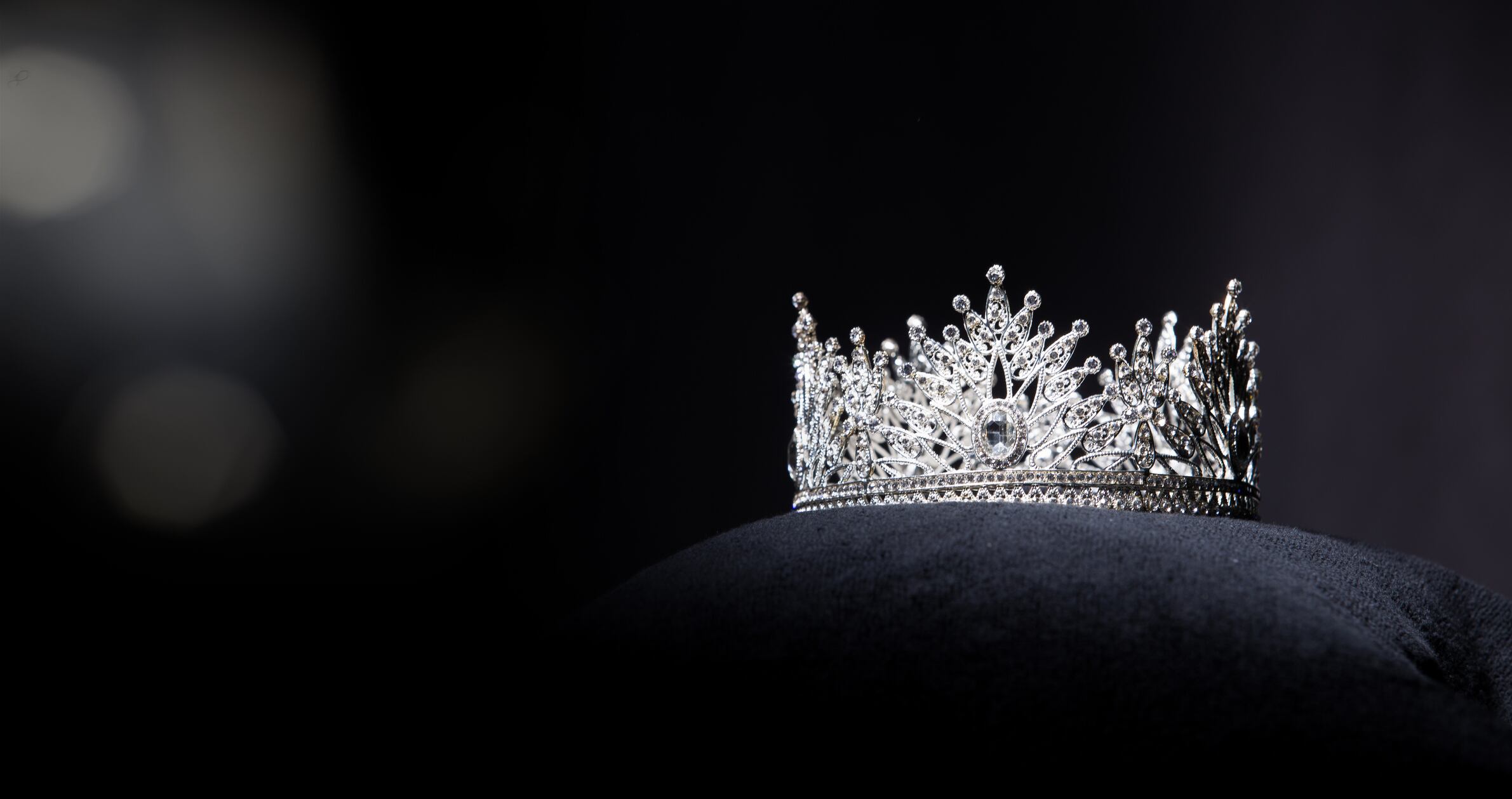 Diamond Silver Crown for Miss Pageant Beauty Contest, Crystal Tiara jewelry decorated gems stone and abstract dark background on black velvet fabric cloth, Macro photography copy space for text logo Cortesía Jade