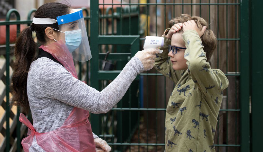 Docentes ingleses toman la temperatura de grupos de niños que asisten presencialmente a sus clases.