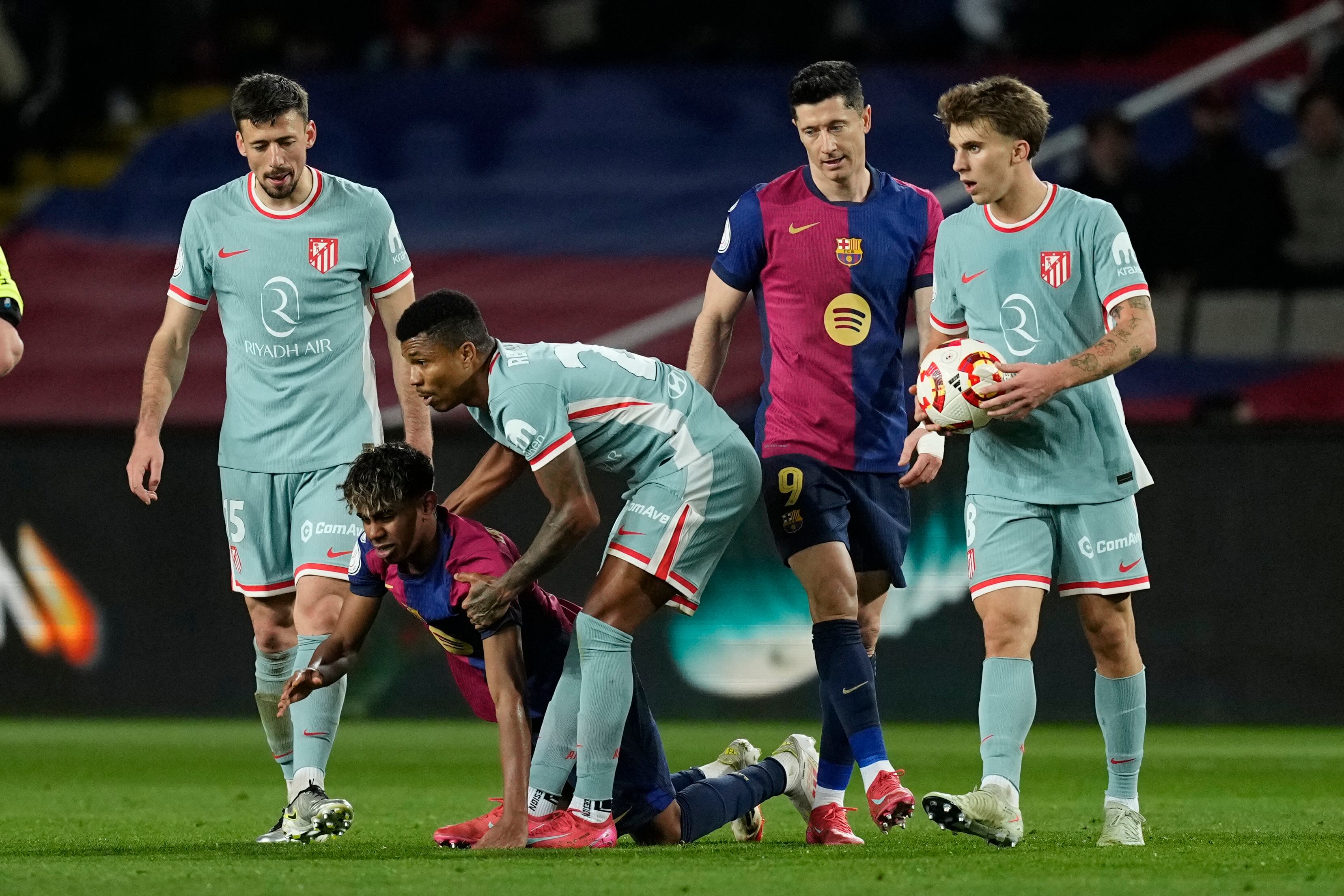 BARCELONA, 25/02/2025.- El defensa del Atlético Reinildo Mandava (c) ayuda a Lamine Lamal (2-i), del Barcelona, durante el partido de ida de las semifinales de la Copa del Rey que FC Barcelona y Atlético de Madrid disputan este martes en el estadio Olímpico Lluis Companys. EFE/Enric Fontcuberta