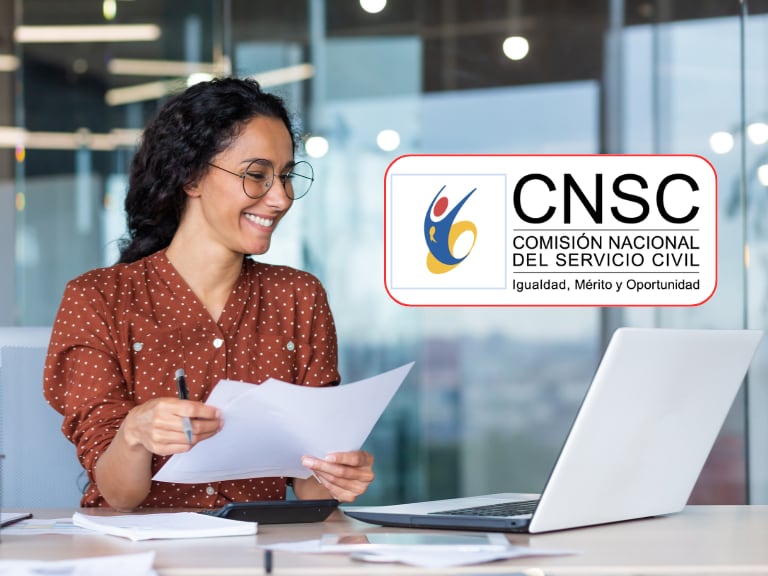 Mujer feliz revisando papeles frente a su computador (Getty Images)