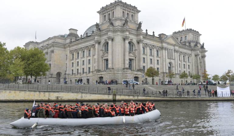 Un total de 121 personas, incluyendo varios diputados alemanes, pasan delante del Parlamento alemán a bordo de una lancha neumatica, que fue utilizada con anterioridad para trasladar refugiados y migrantes, en Berlín.