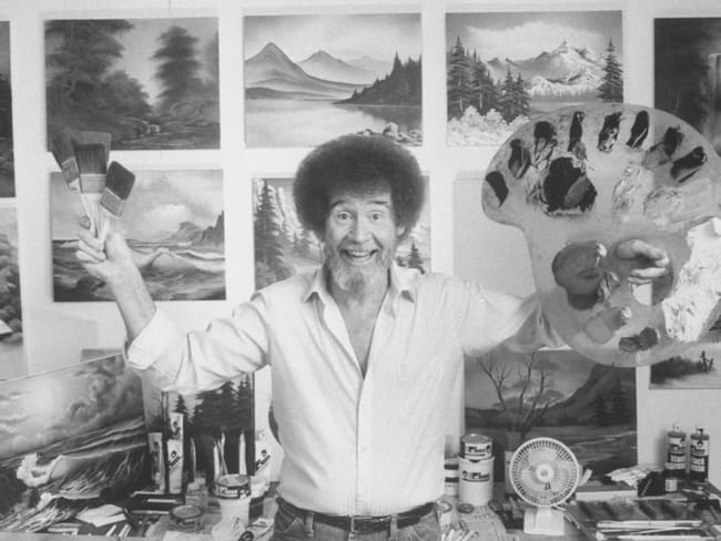TV painting instructor/artist Bob Ross jubiantly holding up paint pallette & brushes as he stands in front of wall covered w. his landscape paintings in his studio. (Photo by Acey Harper/Getty Images)
