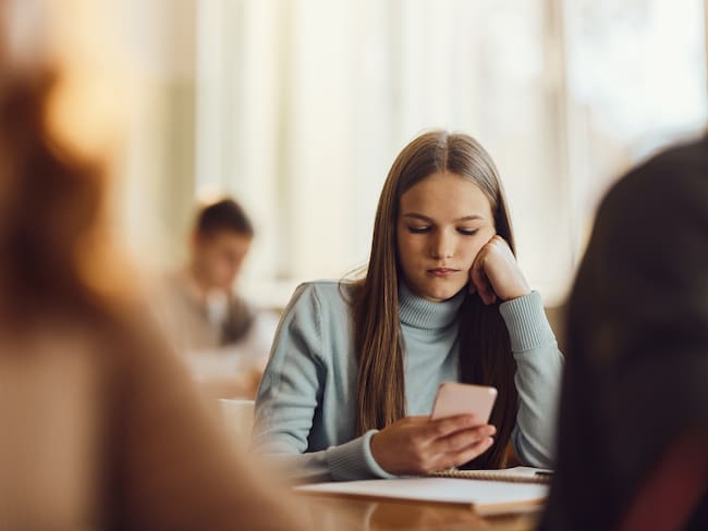 Adolescente revisando su celular mientras está en clase en el colegio (Getty Images)