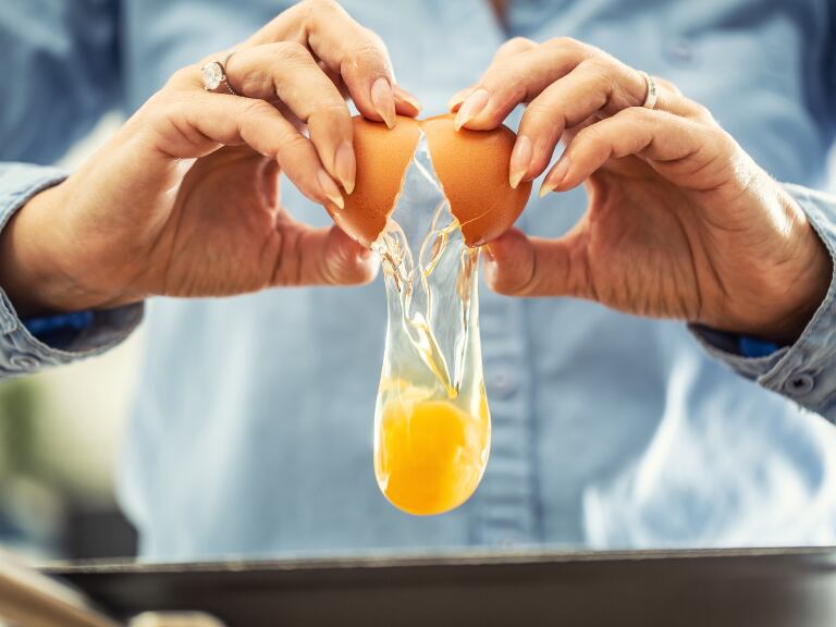 Mujer abriendo un huevo para cocinarlo en un sartén (Getty Images)