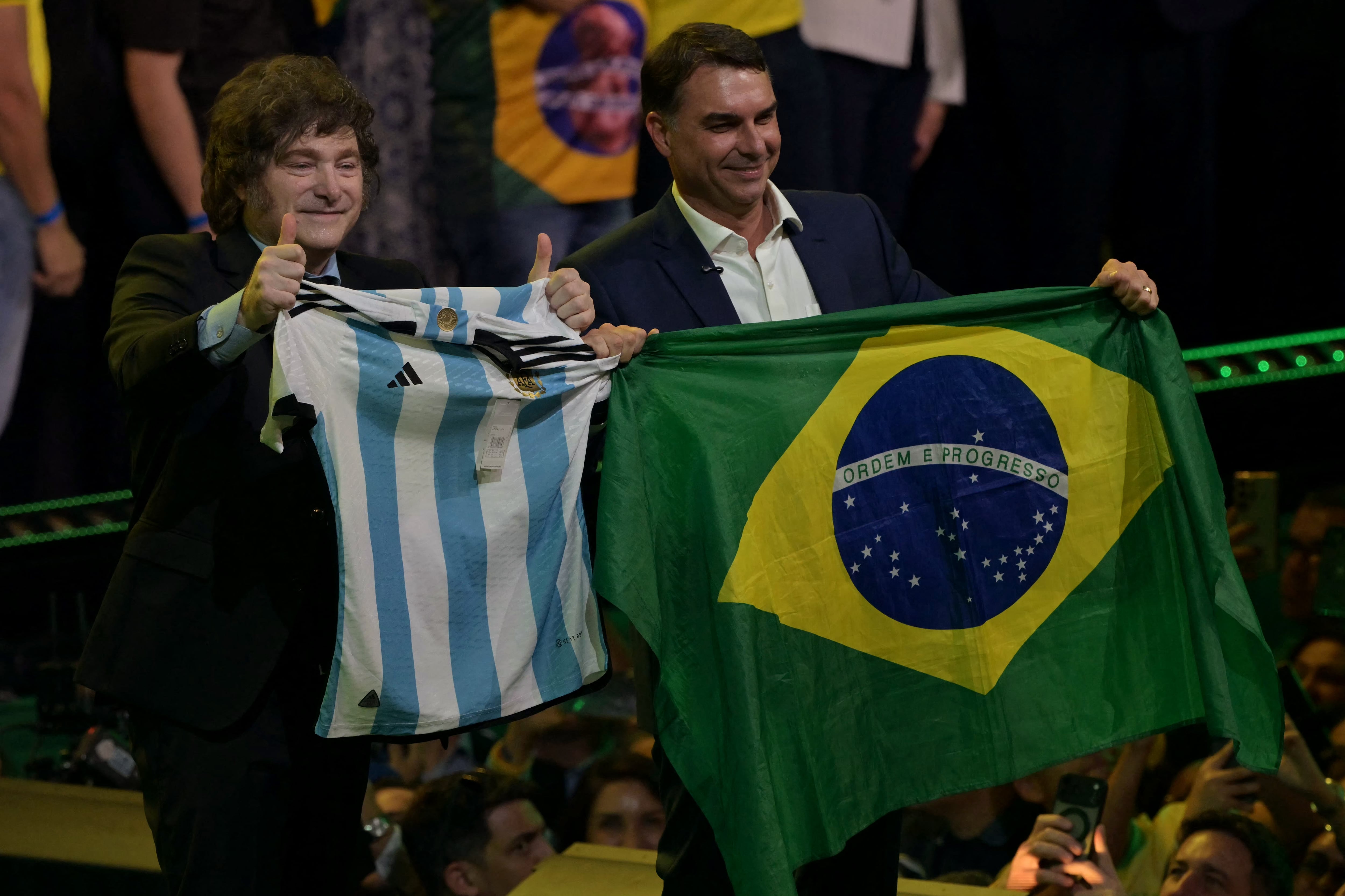 El presidente argentino Javier Milei sostiene una camiseta de la selección nacional de fútbol junto al aspirante presidencial de derecha de Brasil, Flavio Bolsonaro, quien sostiene una bandera nacional, durante el lanzamiento de la candidatura de este último en la convención del Partido Liberal, en São Paulo, Brasil, el 25 de julio de 2026. Aquejado por una serie de crisis políticas, Flavio Bolsonaro lanzó su candidatura para las elecciones presidenciales brasileñas de octubre, buscando seguir los pasos de su padre, Jair Bolsonaro, quien se encuentra bajo arresto domiciliario por planear un golpe de Estado tras perder las elecciones en 2022. (Foto de Nelson ALMEIDA / AFP)