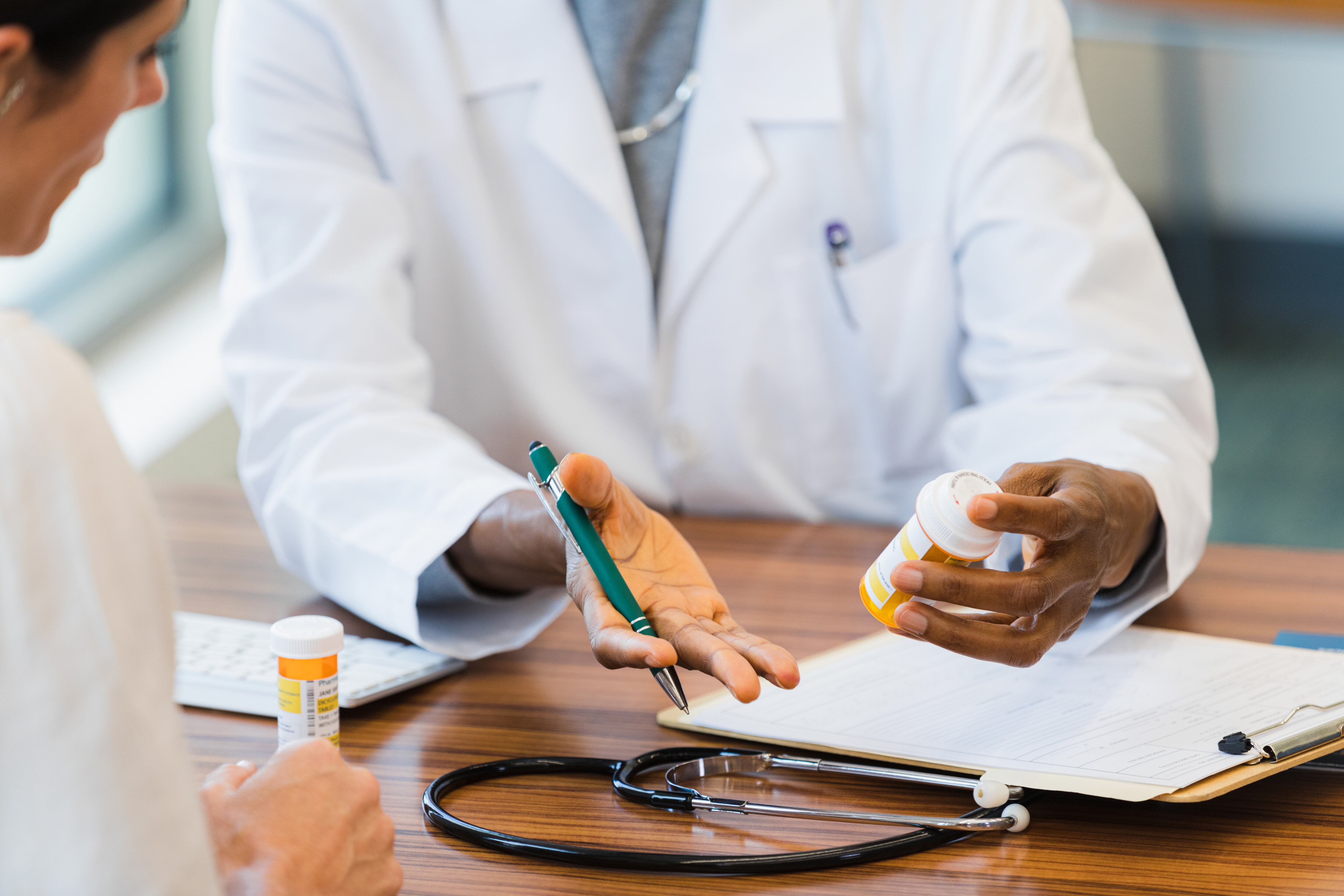An unrecognizable female doctor gestures as she discusses a medication's instructions and side effects. The patient attentively listens to the doctor.