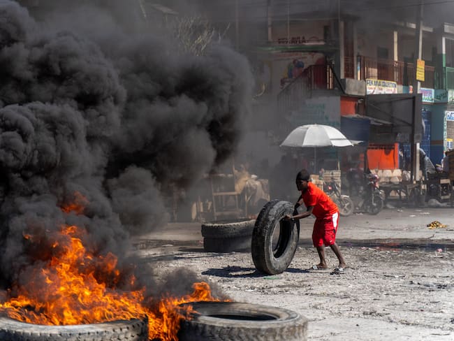 TOPSHOT - A protestor adds a tire to a burning barricade during a police demonstration to protest the recent killings of six police officers by armed gangs, in Port-au-Prince, Haiti, January 26, 2023. - The attacks, which left six officers dead, occurred on January 25 in the town of Liancourt, when officers had to repel four attacks by the gunmen as they tried to take over the station, according to local news. (Photo by Richard Pierrin / AFP) (Photo by RICHARD PIERRIN/AFP via Getty Images)