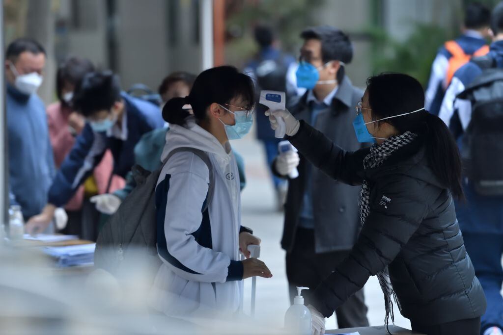 GUANGZHOU, CHINA - DECEMBER 12: A teacher measures body temperature of a student at the entrance of Guangzhou Tianhe Middle School on December 12, 2022 in Guangzhou, Guangdong Province of China. Students with negative nucleic acid test results within 48 hours can return to school in batches and staggered time in Guangzhou as the city optimized COVID-19 control measures. (Photo by Chen Yihang/VCG via Getty Images)