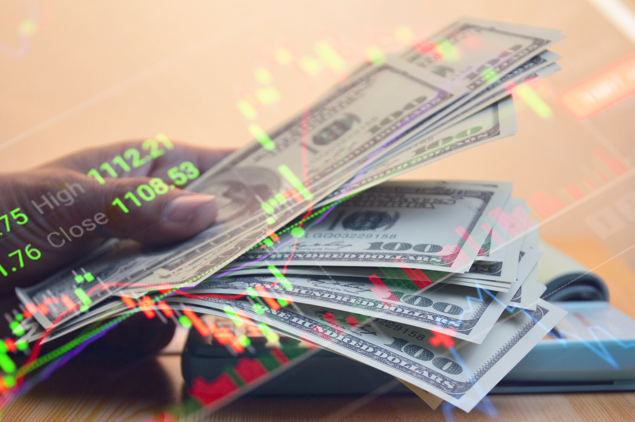 Hombre contando dólares en su mano, sobre una gráfica de los índices de mercado actuales (Getty Images)