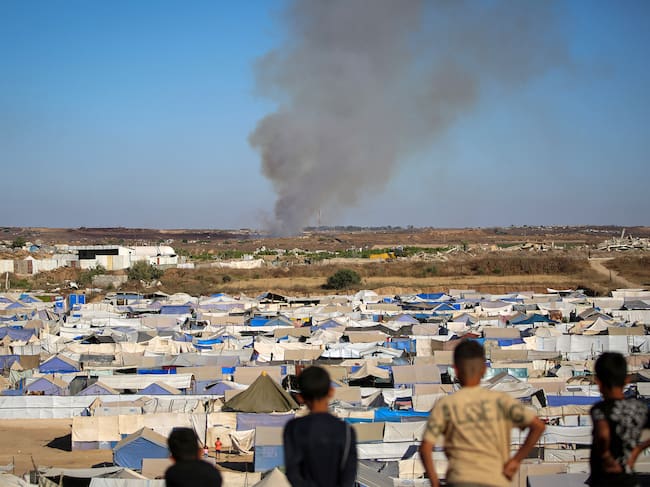 Children watch from atop a promontory overlooking shelters for people displaced by war, as smoke billows in the background near the Nuseirat camp for Palestinian refugees in the central Gaza Strip on June 19, 2026. Palestinian Islamist movement Hamas on Monday hailed a deal between the United States and Iran, expressing hope it would help put an end to violence in the Gaza Strip. Israel and Hamas trade near-daily accusations of truce violations and the Gaza Strip remains gripped by bloodshed as progress on permanently ending the war remains stalled. (Photo by Eyad Baba / AFP)