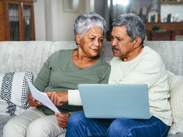 Pareja de adultos mayores revisando sus papeles, mientras la mujer lo mira con preocupación (Getty Images)