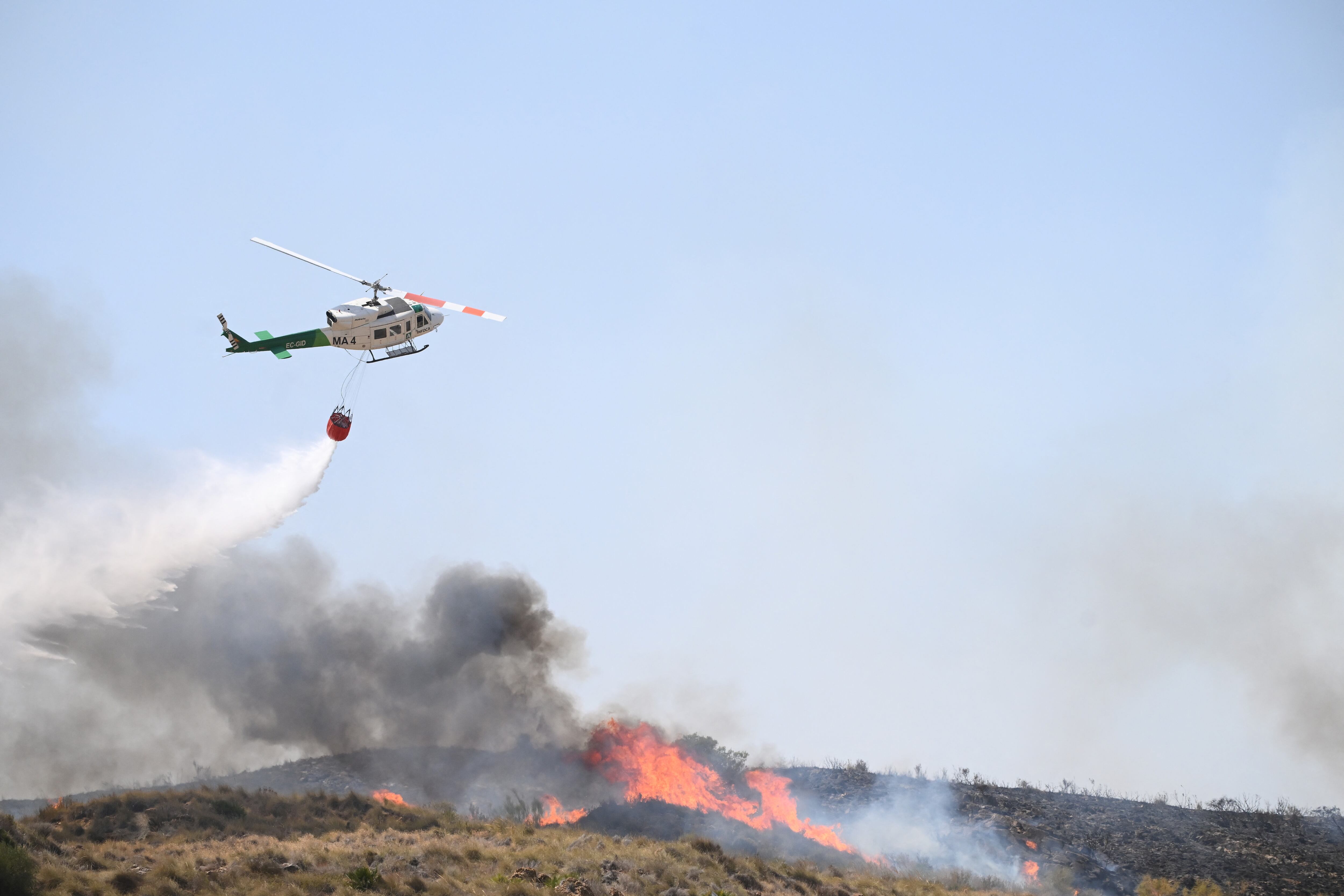 A picture taken on July 10, 2026 shows a helicopter droping water in the area of a wildfire that killed 11 near Los Gallardos, in Almeria Province. Eleven people were killed and 19 are missing after a wildfire in Bedar, in Los Gallardos district, with four victims who may have been British who were burned in their car, authorities said. (Photo by JOSE JORDAN / AFP)