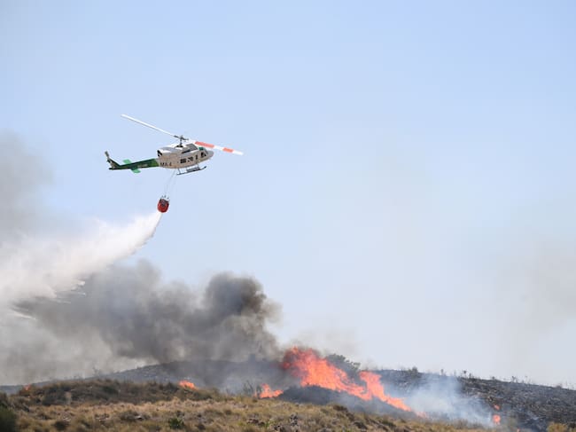 A picture taken on July 10, 2026 shows a helicopter droping water in the area of a wildfire that killed 11 near Los Gallardos, in Almeria Province. Eleven people were killed and 19 are missing after a wildfire in Bedar, in Los Gallardos district, with four victims who may have been British who were burned in their car, authorities said. (Photo by JOSE JORDAN / AFP)