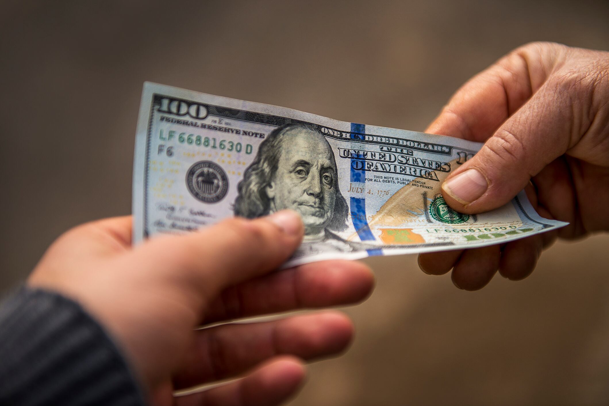 Persona entregando un dólar estadounidense a otra persona en la calle (Getty Images)