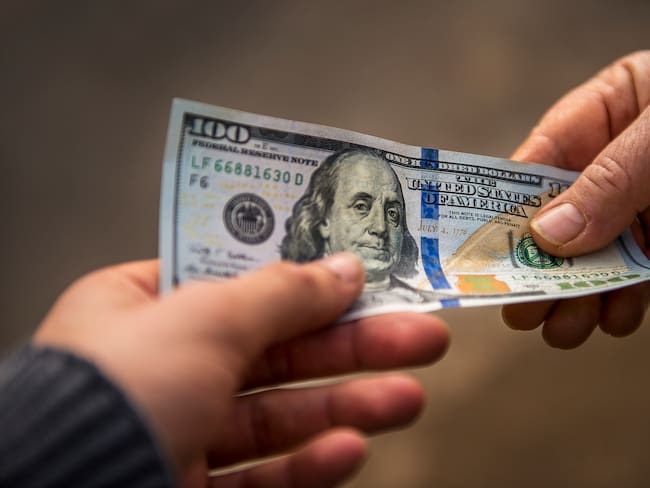 Persona entregando un dólar estadounidense a otra persona en la calle (Getty Images)