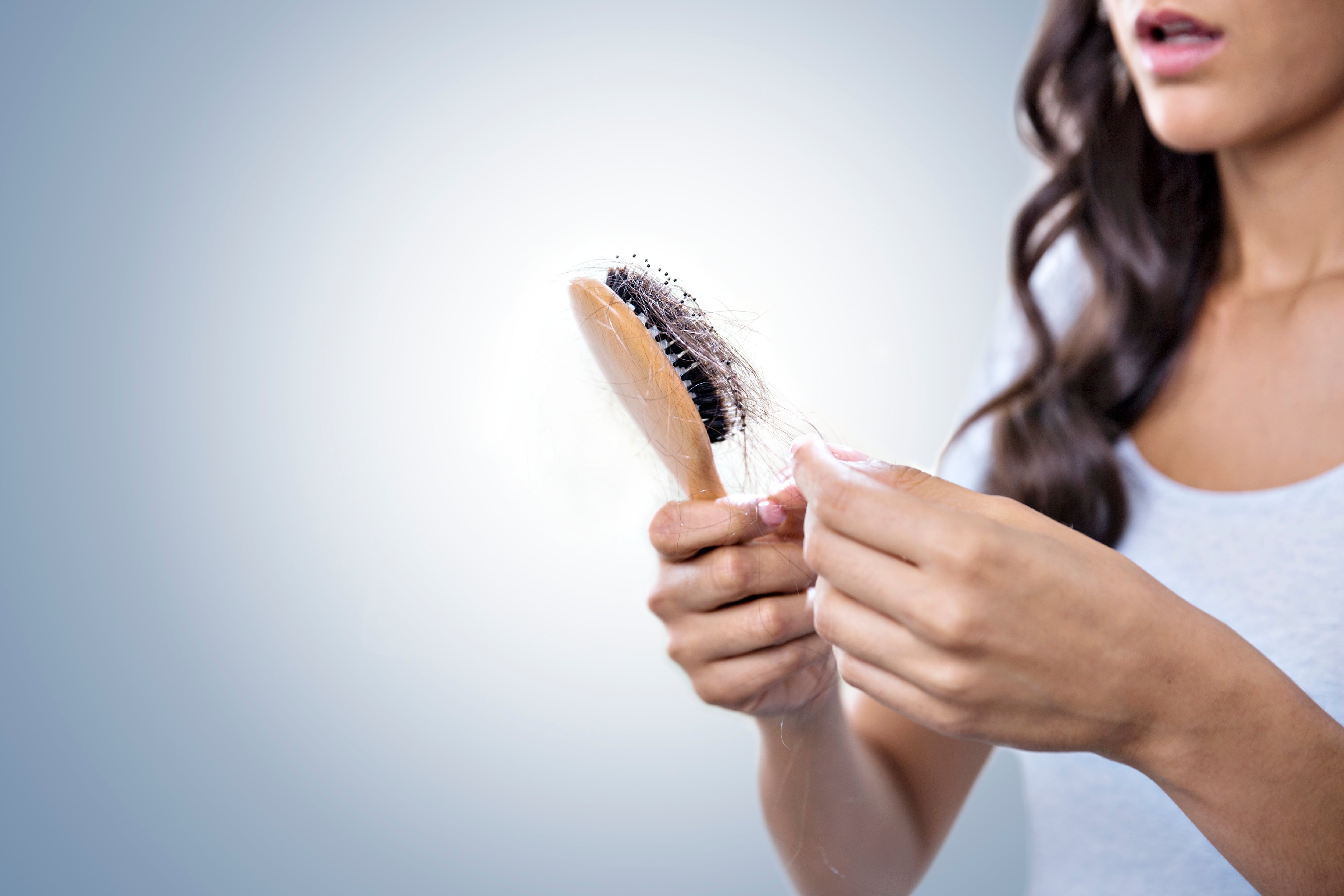 Worried woman holding hairbrush full of hair.