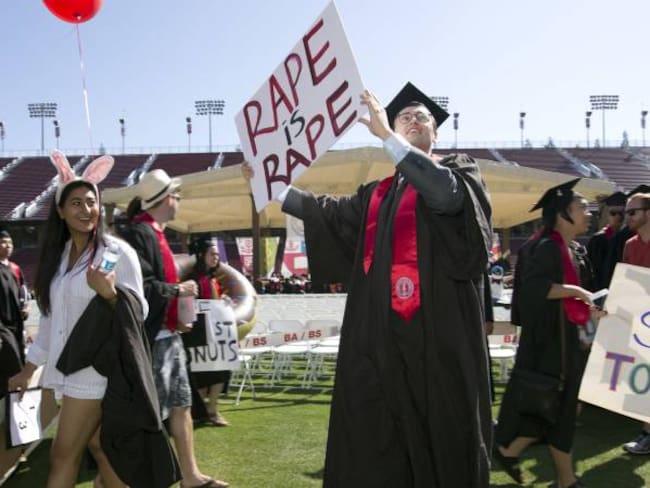 Paul Harrison, centro, lleva un cartel con el texto &quot;violación es violación&quot; en el estadio de Stanford, California.