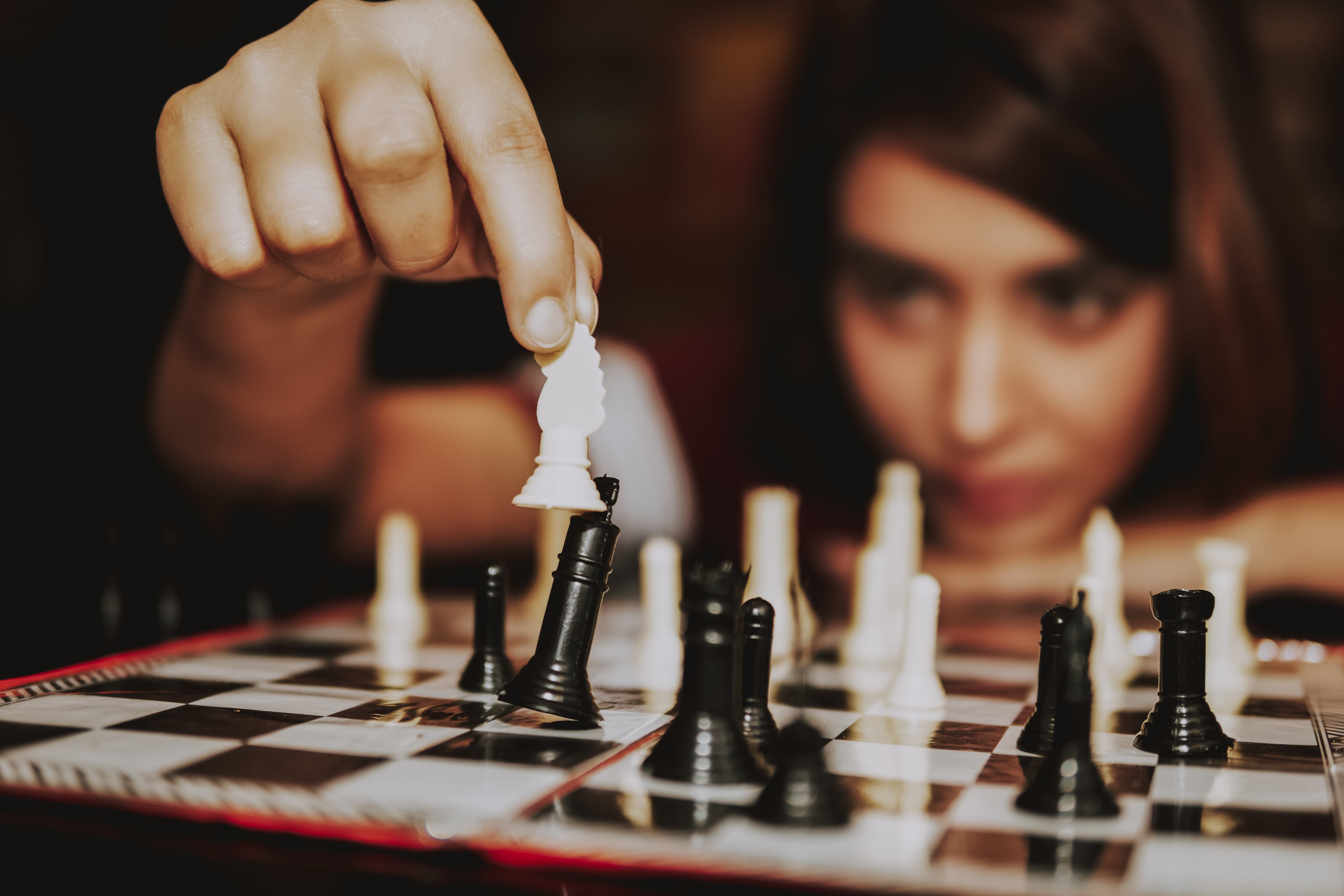 Young woman is making move in a game of Chess. Focus on her hand and chess piece.