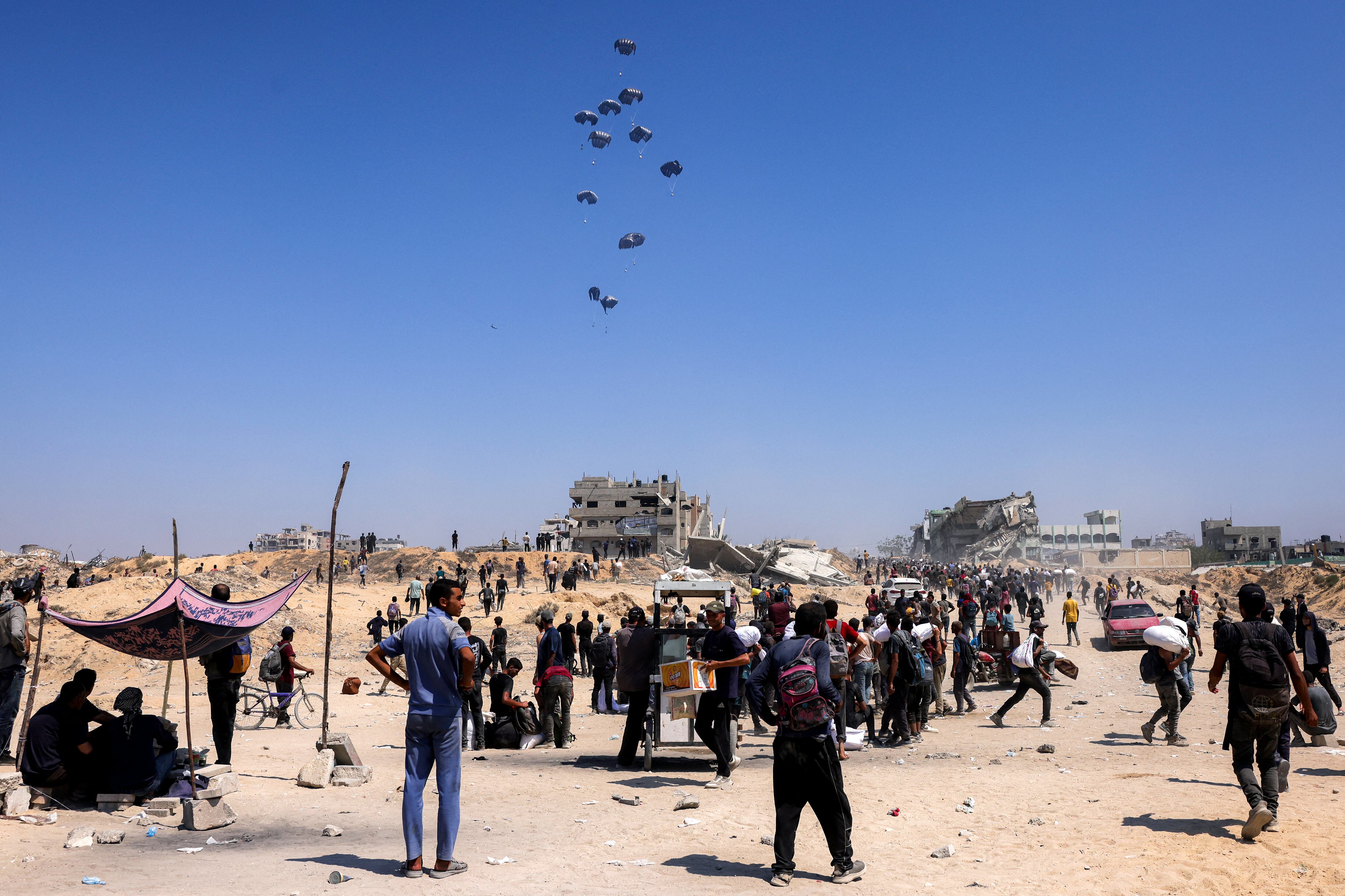 People gather as a C-130 Hercules military transport aircraft drops humanitarian aid on the northern Gaza Strip on July 27, 2025. Two Jordanian and one Emirati plane on dropped 25 tonnes of humanitarian aid over the Gaza Strip, Jordanian state television reported on July 27. (Photo by BASHAR TALEB / AFP)