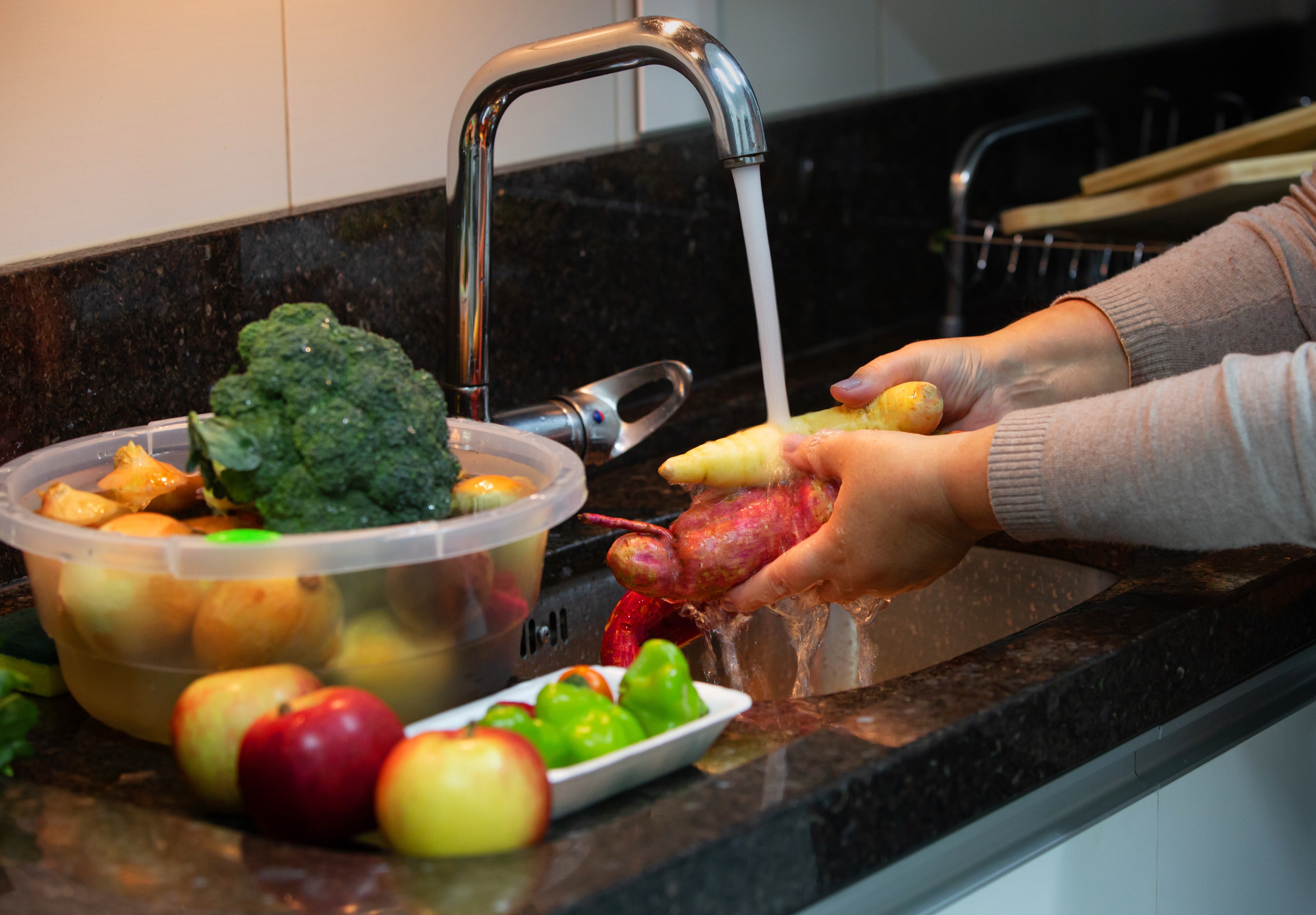 Persona en la cocina lavando las frutas y verduras antes de pelarlas (Foto vía Getty Images)