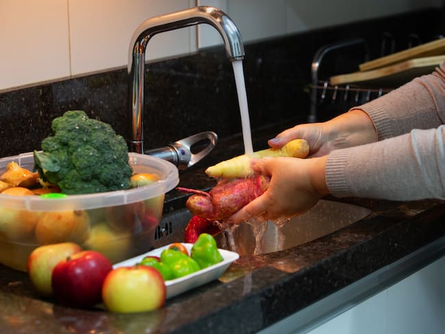 Persona en la cocina lavando las frutas y verduras antes de pelarlas (Foto vía Getty Images)