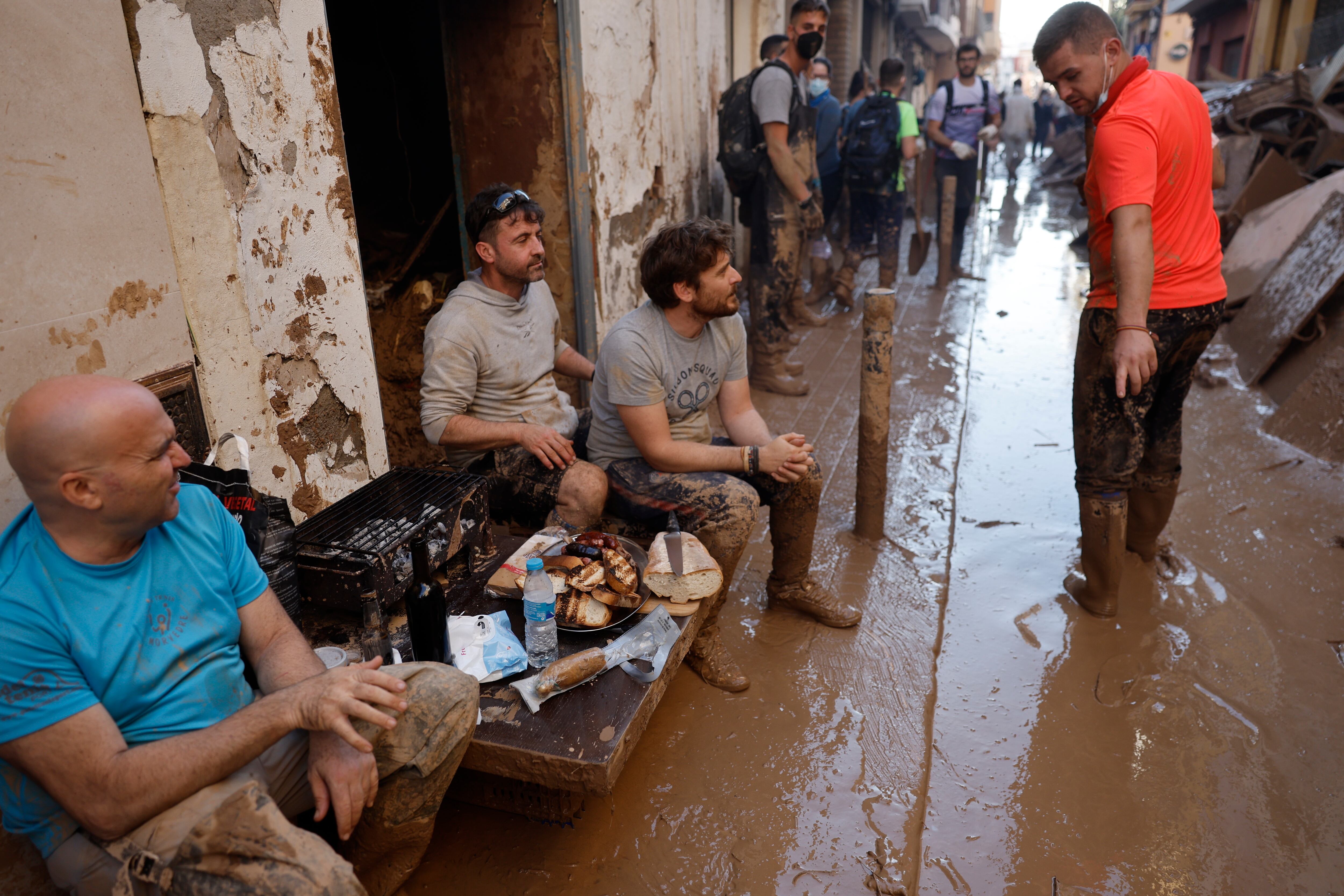 PAIPORTA (VALENCIA), 02/11/2024.- Varias personas comen algo de comida entre el lodo en una calle la localidad valenciana de Paiporta, este sábado. Por tercer día consecutivo una marea de voluntarios ha llegado este sábado a barrios del sur de la ciudad de València y a los pueblos de la comarca vecina de lHorta Sud asolados por la dana para luchar contra un fango, donde grupos especializados de los equipos de intervención buscan cadáveres en garajes o fosos aún anegados.EFE/ Kai Försterling