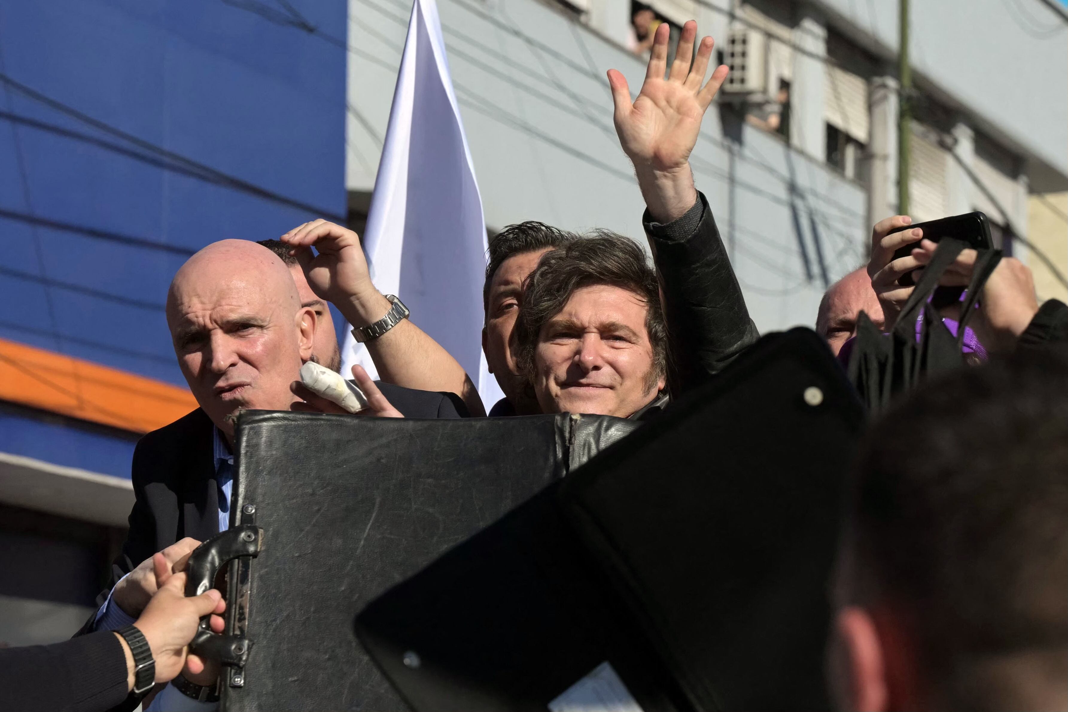 El presidente de Argentina, Javier Milei, su hermana y secretaria general de la presidencia, Karina Milei y el candidato oficialista al congreso, Jose Luis Espert, protegidos detrás de una barrera ante los ataques de manifestantes. 
(Foto:   JUAN MABROMATA/AFP via Getty Images)