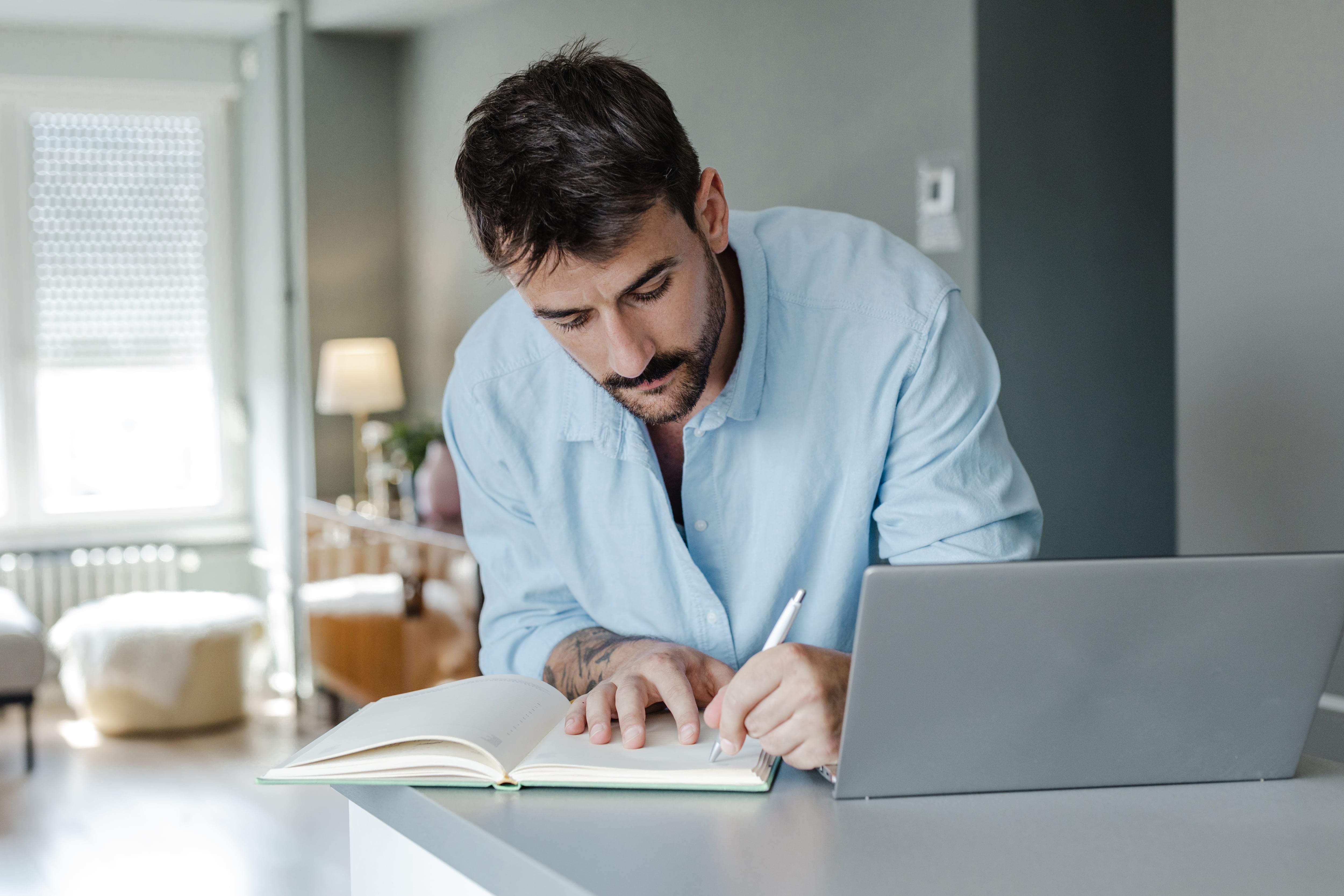 Hombre escribiendo muy rápido en su cuaderno mientras tiene el computador al lado (Getty Images)
