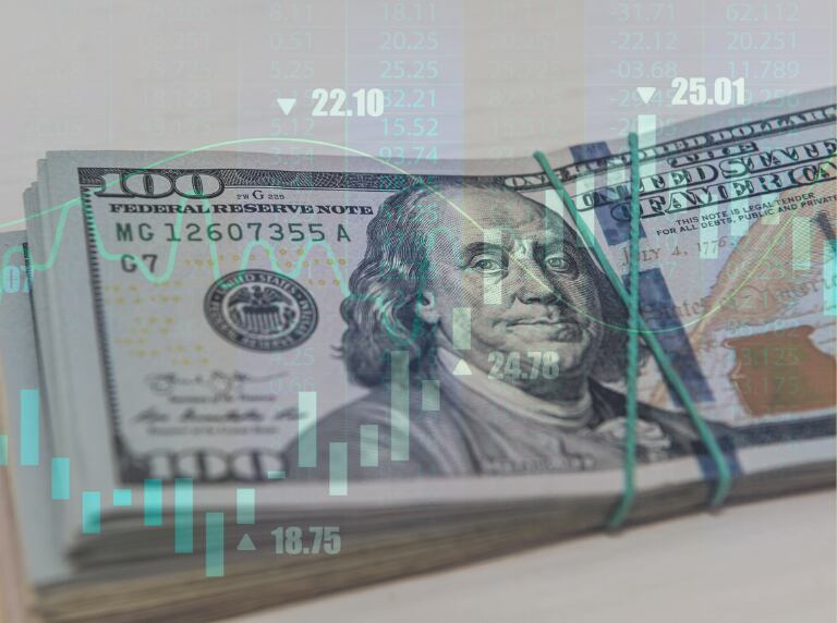 Fajo de dólares estadounidense por detrás de una gráfica de indicadores económicos (Getty Images)