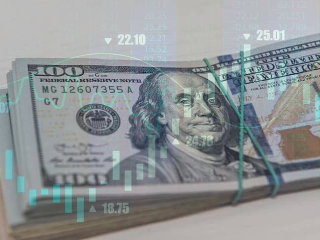 Fajo de dólares estadounidense por detrás de una gráfica de indicadores económicos (Getty Images)
