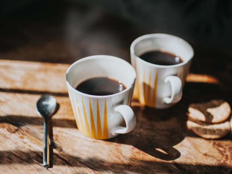 Dos tazas de café sobre una mesa de madera y junto a una cucharita de metal (Getty Images)