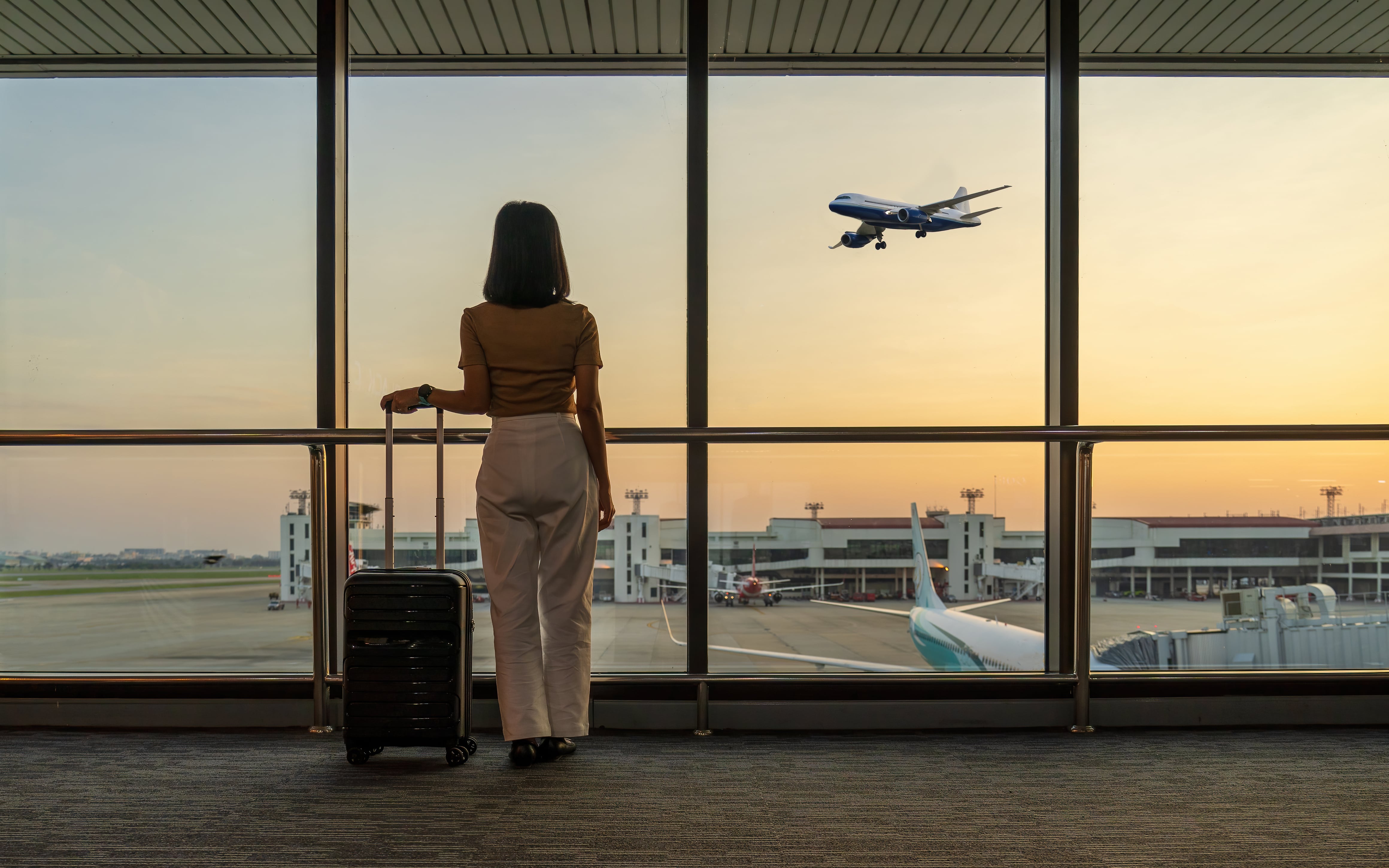 Mujer en un aeropuerto mirando un avión despegar, mientras espera en la puerta de embarque / Foto: GettyImages