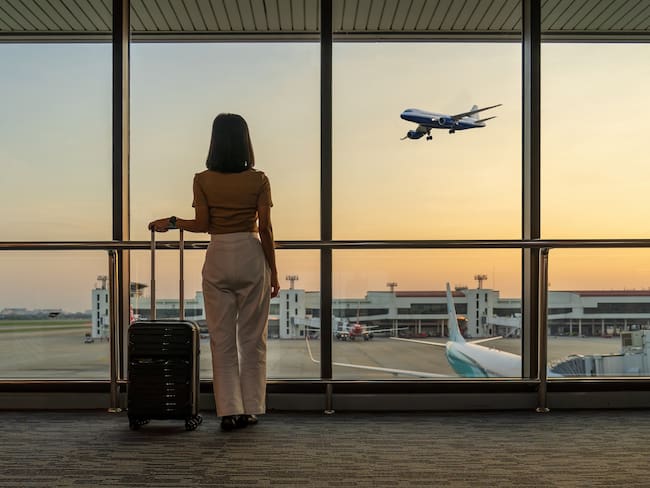 Mujer en un aeropuerto mirando un avión despegar, mientras espera en la puerta de embarque / Foto: GettyImages
